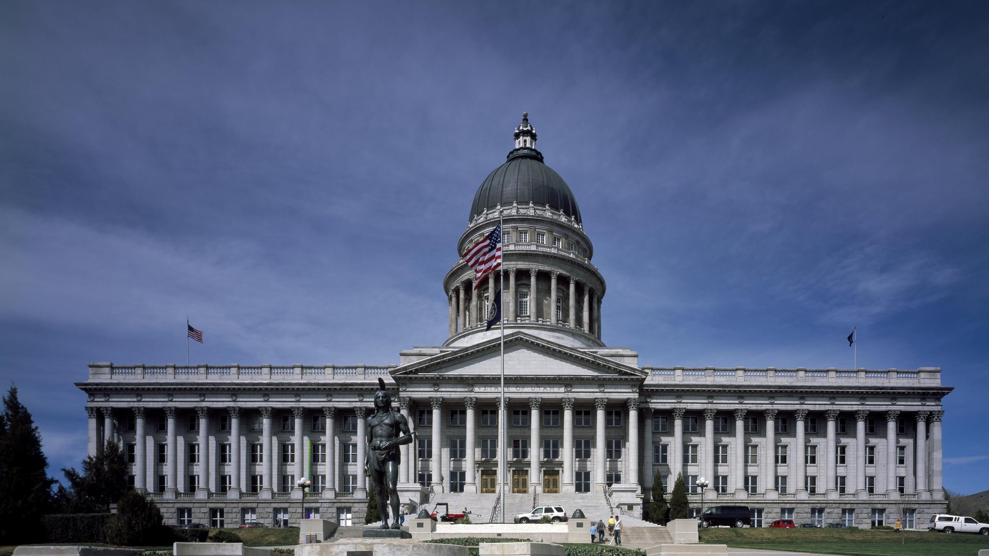 Utah State Capitol -- full dome, portico, flag and the Chief Massasoit statue, frontal elevated approach, clean deep-blue daylight -- SLC’s single most unmistak